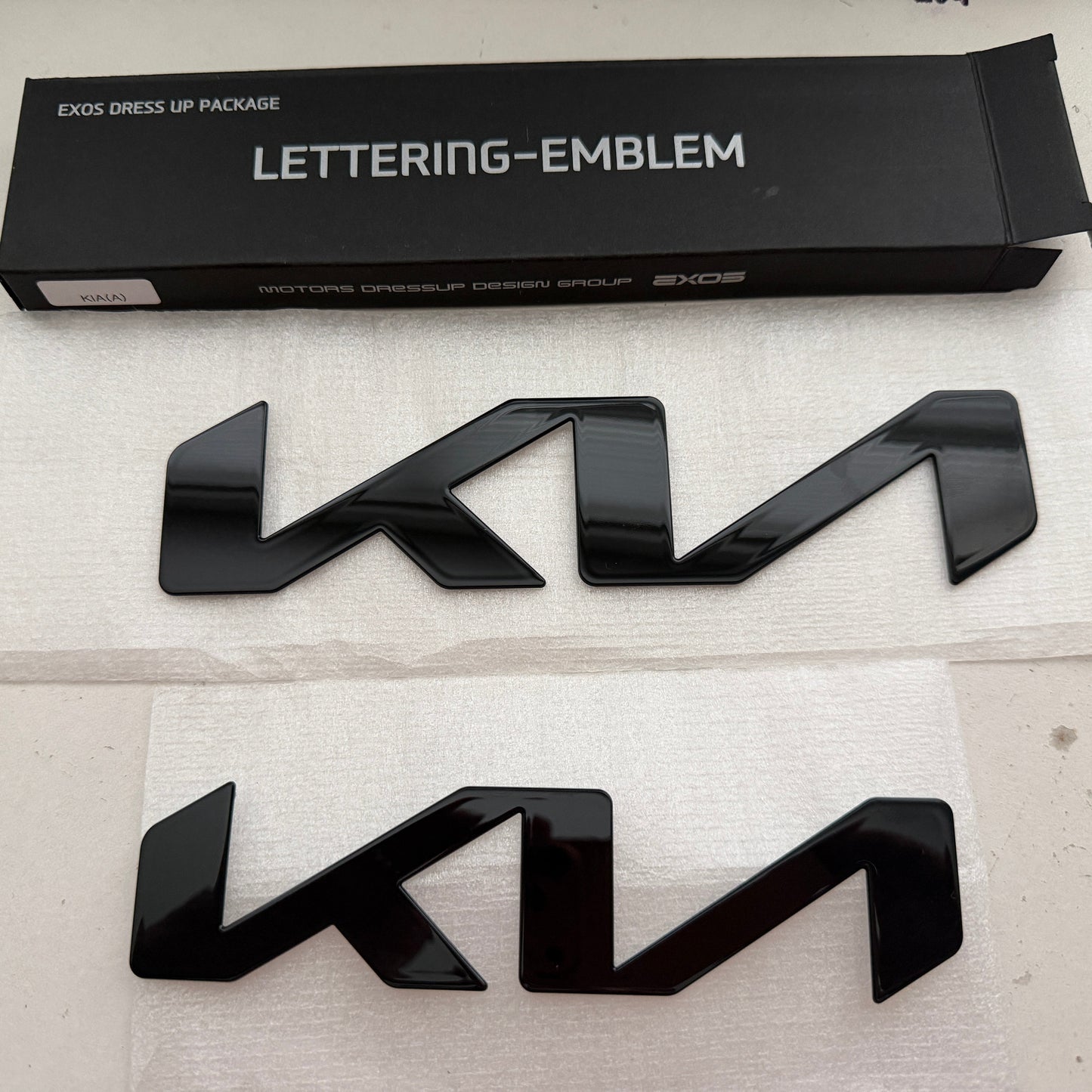 Black KIA lettering emblem with packaging on a light gray background