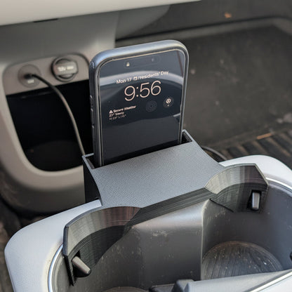 Phone in a car cup holder with digital display showing time and date.